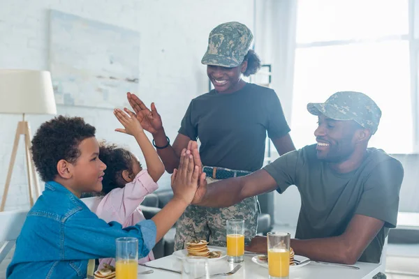 Parents in camouflage clothes giving five to their children by kitchen table — Stock Photo