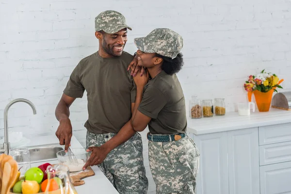 Жінка і чоловік у військовій формі обіймається на кухні — стокове фото