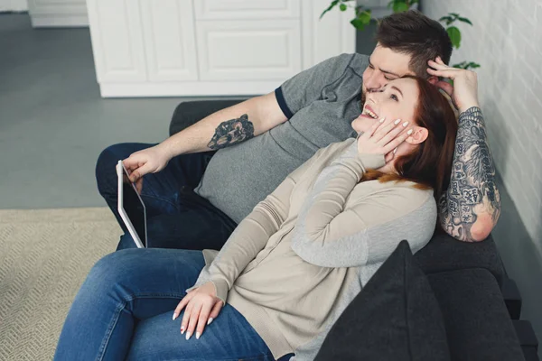 Lachender Freund und Freundin auf dem Sofa liegend und zu Hause etwas auf dem Tablet gucken — Stockfoto