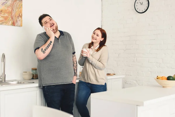 Glücklicher Freund spricht per Smartphone und Freundin hält Tasse Kaffee in der Küche — Stockfoto