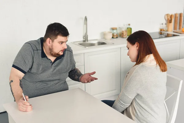 Overweight boyfriend quarreling with girlfriend and holding smartphone in kitchen — Stock Photo