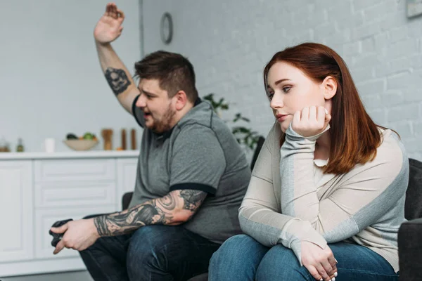 Sad girlfriend sitting on sofa while boyfriend playing video game at home — Stock Photo
