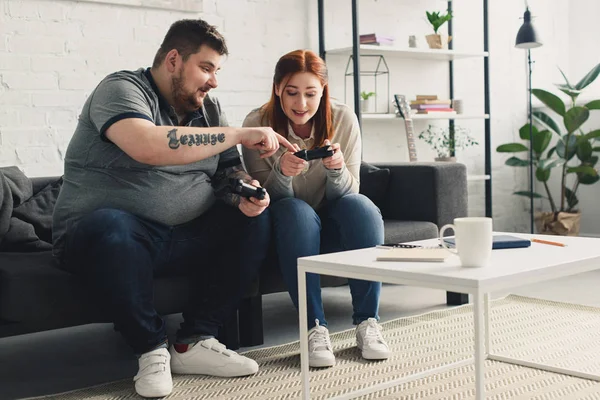 Boyfriend pointing on gamepad to girlfriend at home — Stock Photo