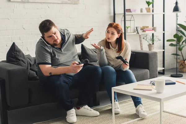 Boyfriend talking by smartphone and girlfriend gesturing to play video game at home — Stock Photo