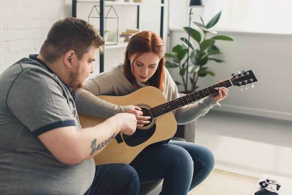 Бойфренд учит девушку играть на акустической гитаре дома — стоковое фото