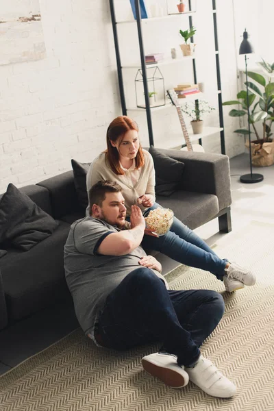 Novio y novia viendo la televisión y comer palomitas de maíz en casa - foto de stock