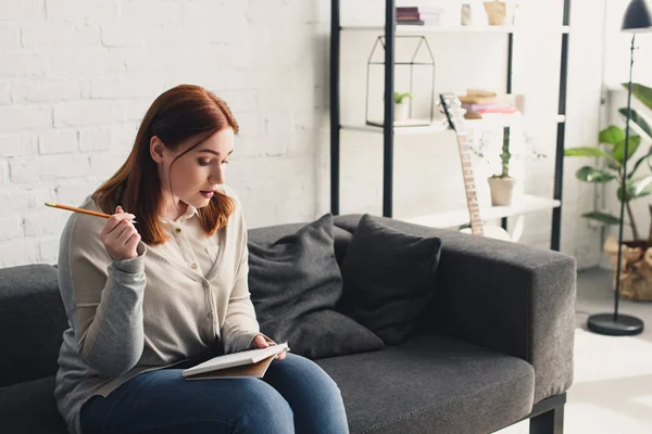 Schönes Mädchen, das Bleistift in der Hand hält und zu Hause etwas in Notizbuch liest — Stockfoto