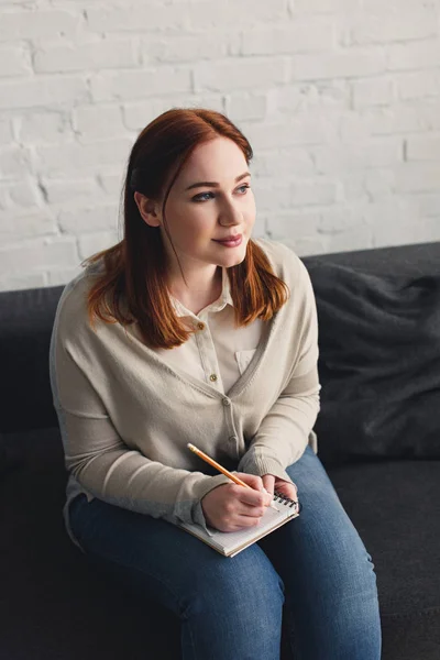 Attractive girl holding notebook and pencil and looking away at home — Stock Photo