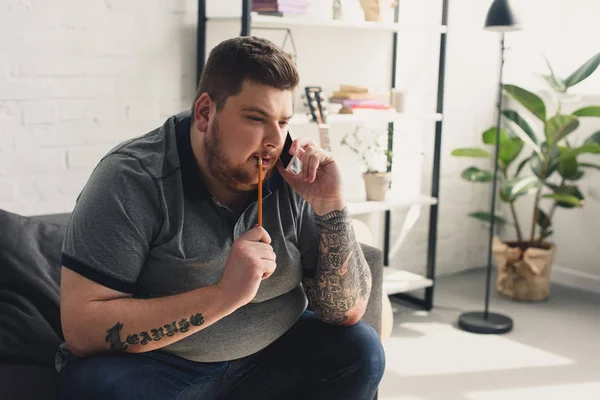 Schöner Mann, der zu Hause mit Smartphone und Bleistift spricht — Stockfoto