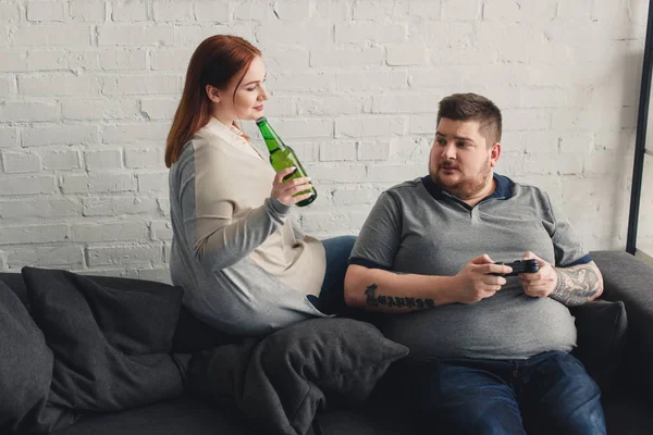 Taille plus petit ami tenant joystick et petite amie tenant bouteille de bière à la maison — Photo de stock