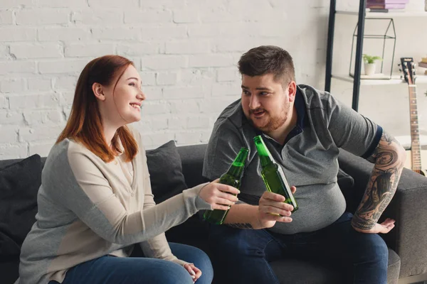 Smiling overweight boyfriend and girlfriend clinking with bottles of beer — Stock Photo