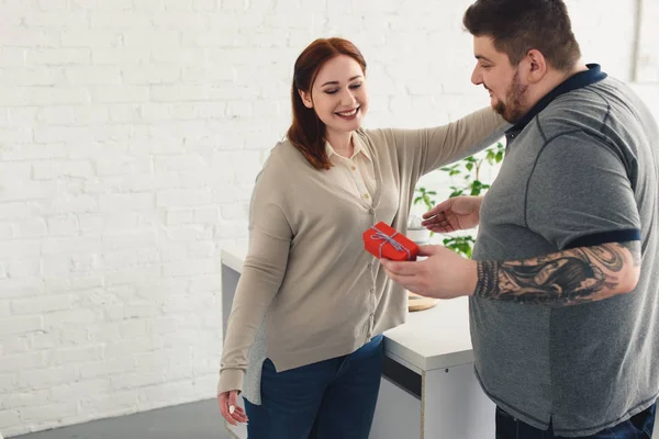 Smiling girlfriend hugging boyfriend for present in kitchen — Stock Photo