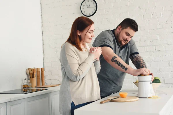 Größe plus Freundin sieht aus, wie Freund zu Hause Orangensaft zubereitet — Stockfoto