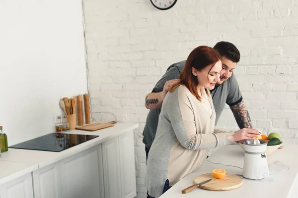 Sobrepeso namorado abraçando namorada enquanto ela fazendo suco na cozinha — Fotografia de Stock