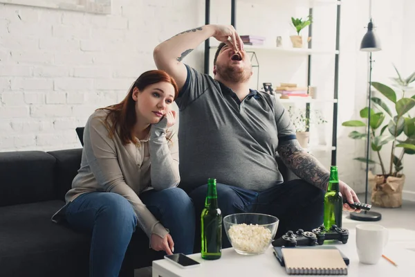 Dimensione più fidanzato mangiare popcorn e stanca ragazza guardando la tv a casa — Foto stock