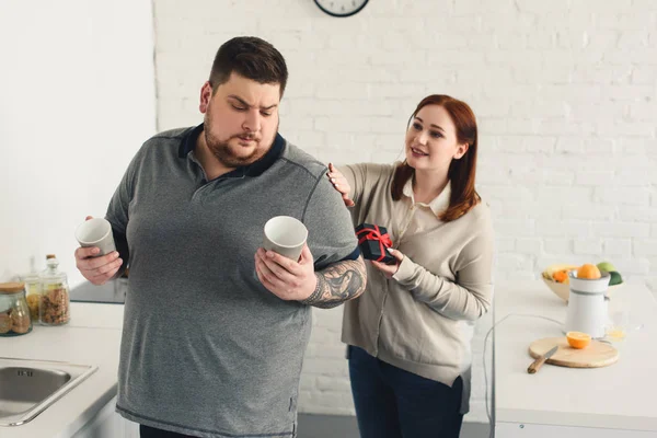 Dimensione più fidanzata che presenta regalo al fidanzato in cucina — Foto stock