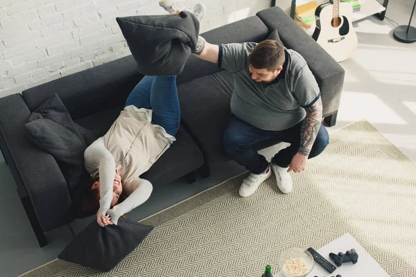 Vista de ángulo alto de novio y novia con sobrepeso luchando con almohadas en casa - foto de stock