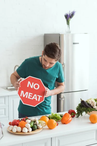 Hombre vegano guapo mirando ningún signo de carne en la cocina - foto de stock