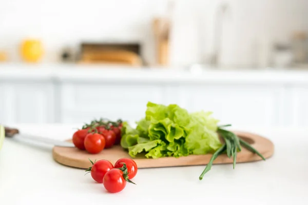 Tomates cereja e folhas de salada na tábua de corte na cozinha — Fotografia de Stock