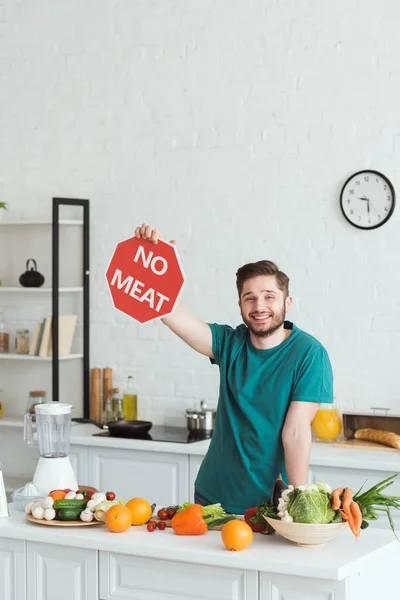 Lächelnder gutaussehender Veganer, der kein Fleischschild in der Küche hält — Stockfoto
