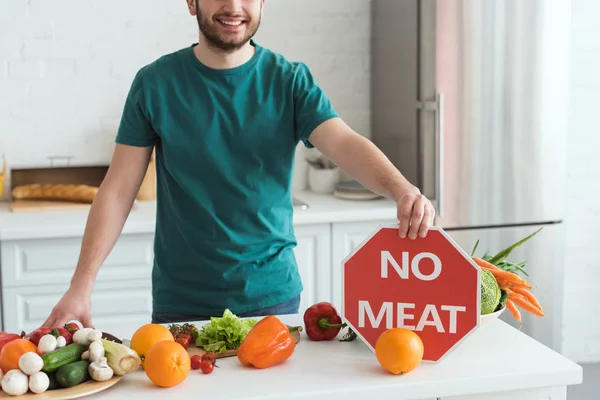 Imagem cortada de belo homem vegan segurando nenhum sinal de carne na cozinha — Fotografia de Stock