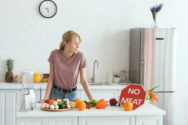Привлекательная веганская девушка смотрит на отсутствие мяса знак на кухне — стоковое фото