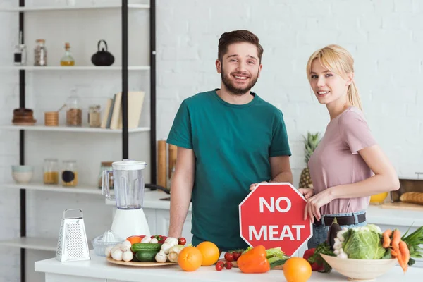 Pareja de veganos sosteniendo ningún signo de carne en la cocina - foto de stock