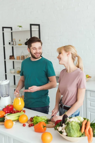 Couple de végétaliens souriant et parlant tout en cuisinant des aliments à la cuisine — Photo de stock