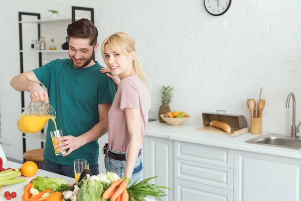 Novio vegano verter jugo fresco en el vidrio en la cocina - foto de stock