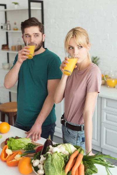 Couple of vegans drinking fresh juice at kitchen and looking away — Stock Photo