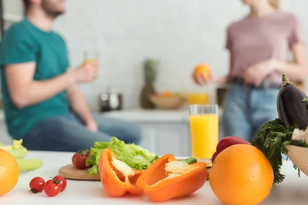 Imagen recortada de pareja vegana hablando en la cocina con frutas y verduras en primer plano - foto de stock