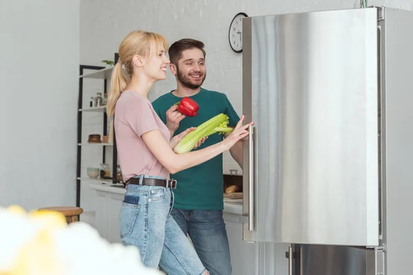 Par de vegans levando legumes da geladeira na cozinha — Fotografia de Stock