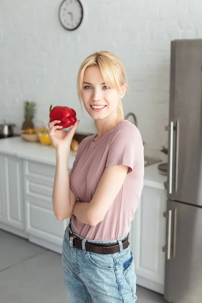 Attractive vegan girl holding bell pepper in kitchen and looking at camera — Stock Photo