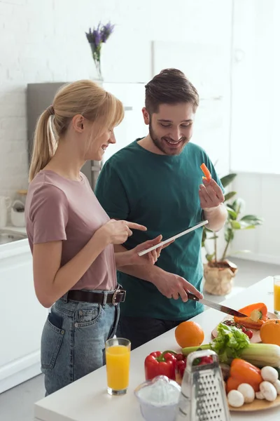 Couple of vegans using tablet with recipe for preparing food at kitchen — Stock Photo