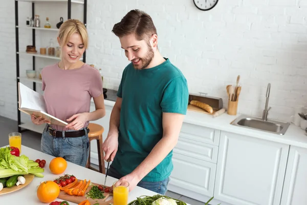 Pareja de veganos cocinando con libro de recetas en la cocina - foto de stock