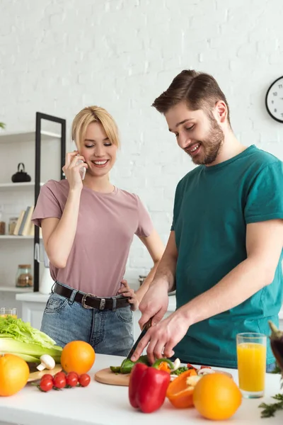 Vegan girlfriend talking by smartphone while boyfriend cooking at kitchen — Stock Photo