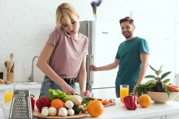 Vegan girlfriend talking by smartphone while cooking salad at kitchen — Stock Photo