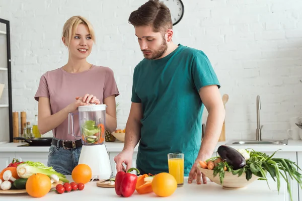 Couple of vegans preparing vegetable juice with juicer at kitchen — Stock Photo