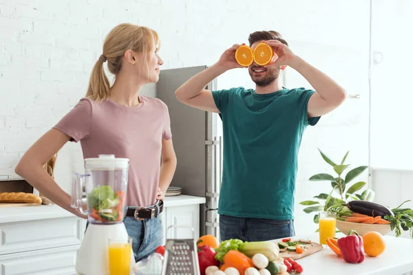 Freund hat Spaß und deckt Augen mit orangefarbenen Stücken in der Küche, veganes Konzept — Stockfoto