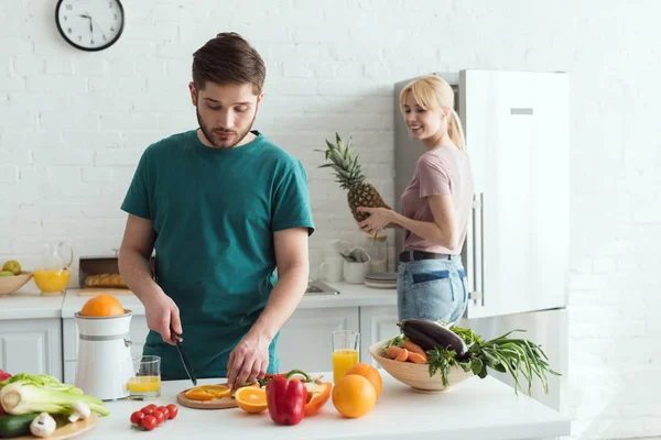 Novio cortar frutas para la comida vegana en la cocina - foto de stock