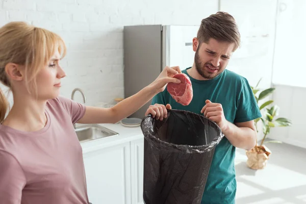 Couple jetant de la viande crue dans la cuisine à la maison, concept de mode de vie végétalien — Photo de stock