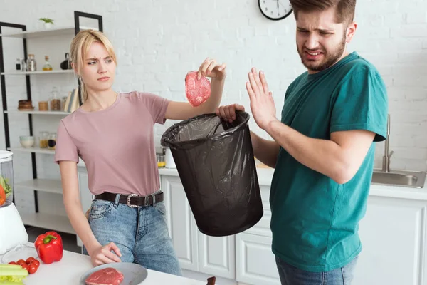 Casal vegan jogando fora carne crua na cozinha em casa — Fotografia de Stock