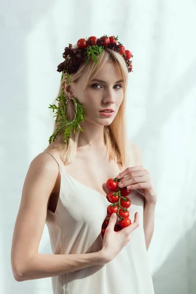 Mujer joven con tomates cherry en las manos y pendientes hechos de rúcula fresca, concepto de estilo de vida vegano - foto de stock