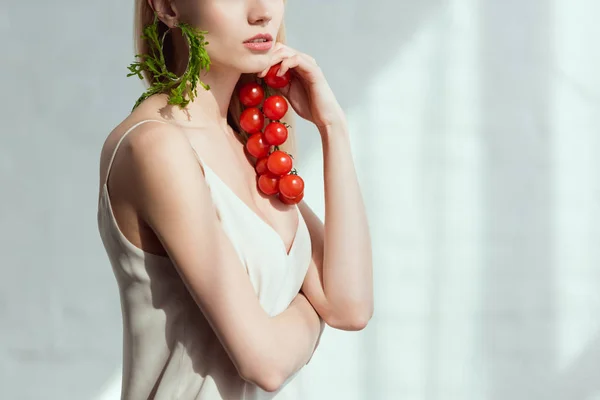Partial view of woman with cherry tomatoes in hand and earring made of fresh arugula, vegan lifestyle concept — Stock Photo