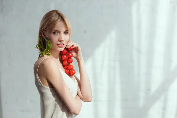 Mujer joven con tomates cherry en la mano y pendientes hechos de rúcula fresca, concepto de estilo de vida vegano - foto de stock