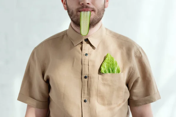 Partial view of man with cucumber slice in mouth and savoy cabbage leaf in pocket, vegan lifestyle concept — Stock Photo