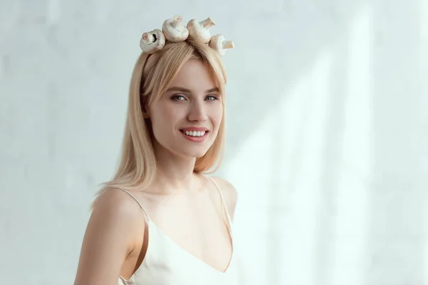Bonita mujer sonriente en vestido con corona hecha de champiñones frescos en la cabeza, concepto de estilo de vida vegano - foto de stock