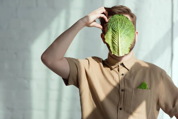 Visão obscurecida do homem pensativo com folha de couve savoy no rosto, conceito de estilo de vida vegan — Fotografia de Stock