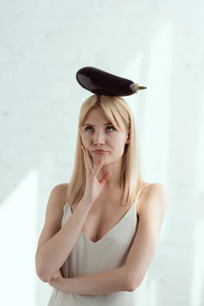 Portrait of young pensive woman with fresh eggplant on head, vegan lifestyle concept — Stock Photo