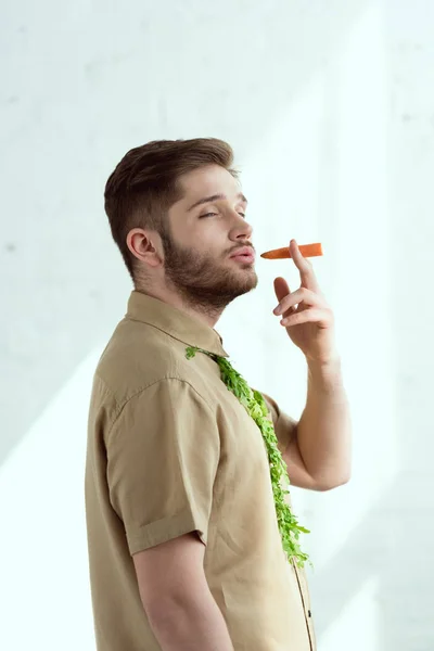 Side view of young man with tie made of arugula and carrot as cigarette, vegan lifestyle concept — Stock Photo